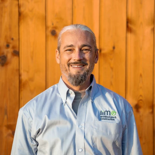 Man wearing a light blue shirt with a logo in front of a wooden fence