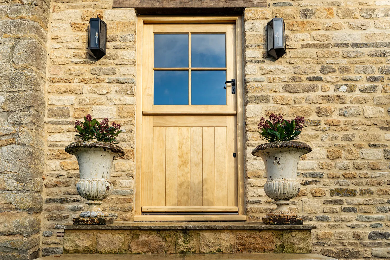 Wooden door with glass panels flanked by stone walls and decorative urns.