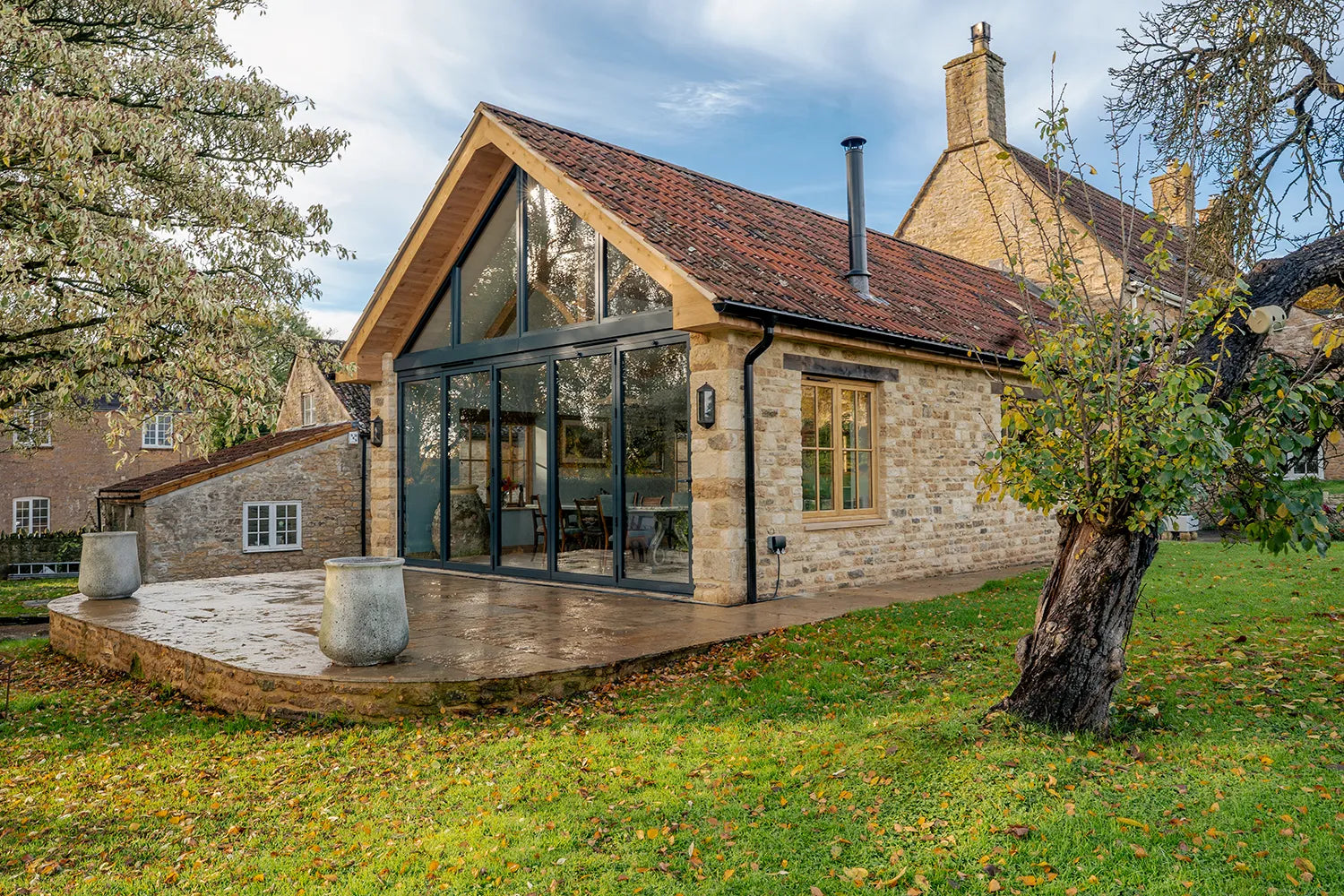Modern house with large glass windows and stone exterior, surrounded by trees and grass.