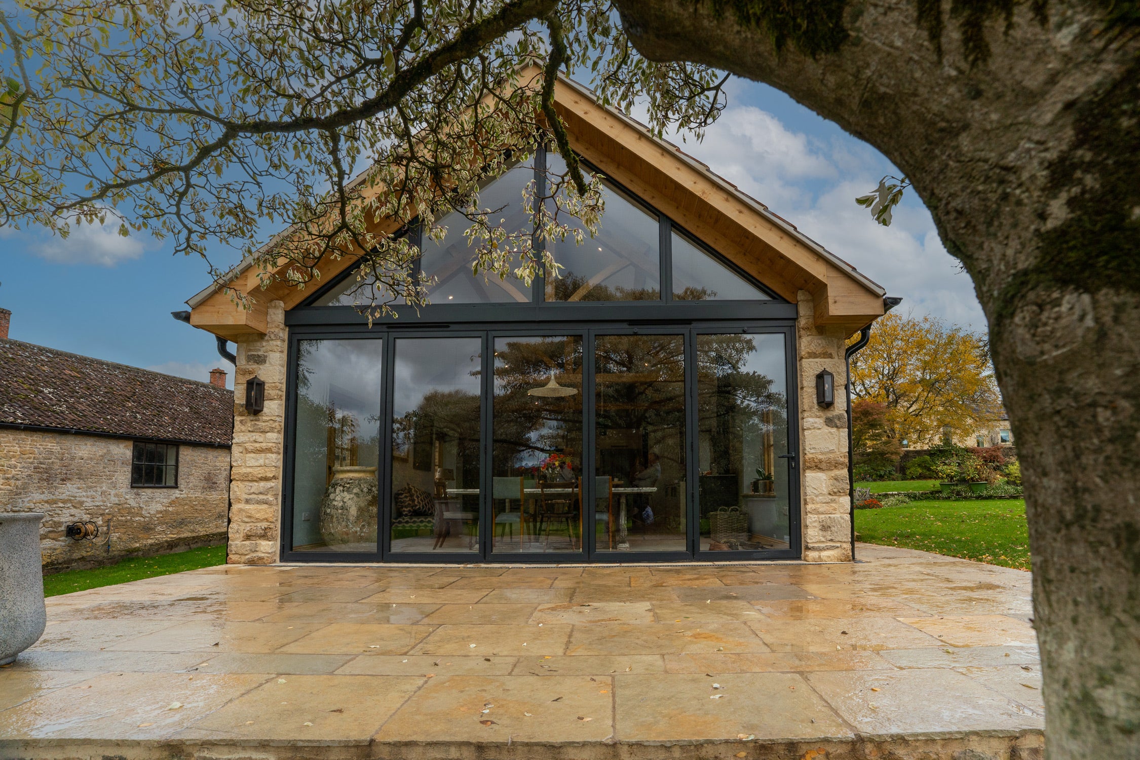 Modern extension of a stone building with large glass windows, surrounded by trees and greenery.